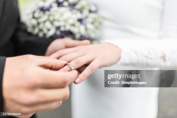 detail of groom putting a ring on a finger of the bride. - metallic dress stock pictures, royalty-free photos & images
