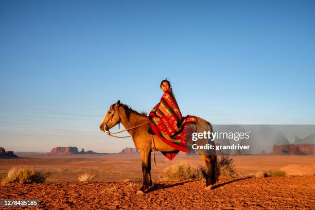 dodici anni vecchia navajo ragazza seduta in cima al suo cavallo di colore bay brown di fronte al famoso buttes nel monument valley tribal park nel nord dell'arizona usa al crepuscolo con una coperta indiana - indian animals foto e immagini stock