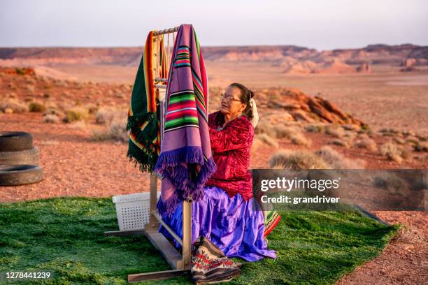 アリゾナ州北部のモニュメントバレー部族公園近くの夕暮れ時の砂漠の本物のネイティブアメリカン織機に伝統的な毛布や敷物を織る高齢のナバホ女性 - ute ストックフォトと画像