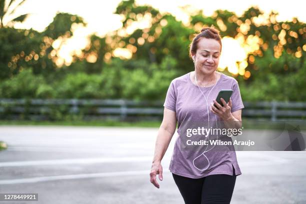 reife frau zu fuß bei sonnenuntergang mit einem handy - park live stock-fotos und bilder