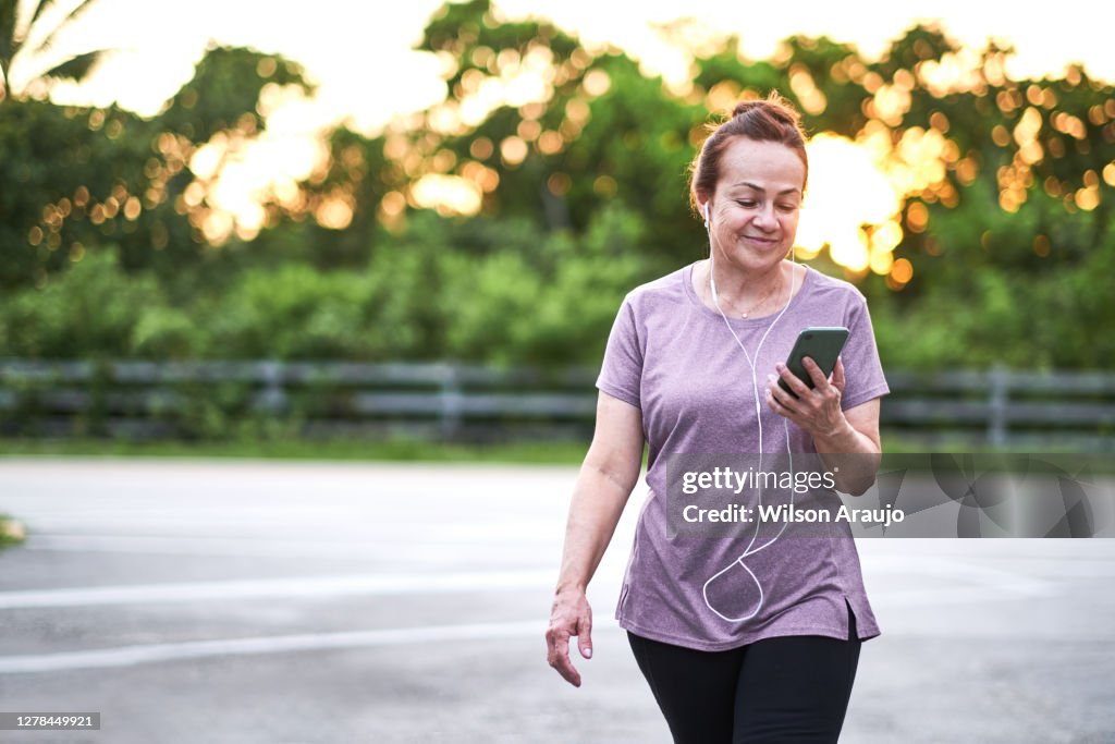 成熟的女人拿著手機在夕陽下行走。