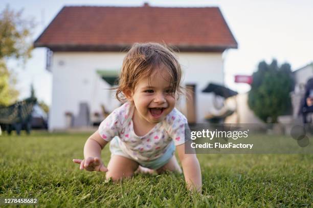 ecstatic baby girl crawling on grass outdoors in a back yard in summer - one and a half summer stock pictures, royalty-free photos & images