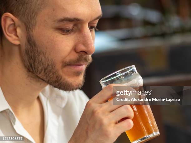 caucasian young man in white shirt drinks red handcraft beer in large glass - alexandre trink stock-fotos und bilder