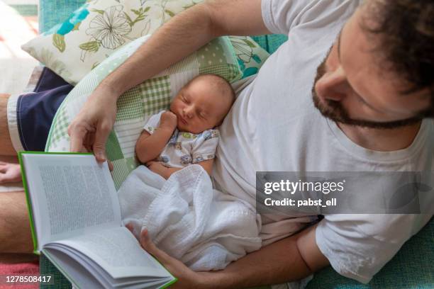 vater liest papierbuch mit baby auf dem schoß - vaterschaft stock-fotos und bilder