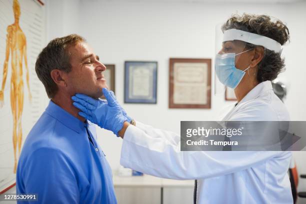 een vrouwelijke arts met beschermende het werkslijtage die een schildkliercontrole doet. - keel stockfoto's en -beelden
