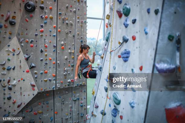 young female athlete suspended from climbing wall in gym - rappelling stock pictures, royalty-free photos & images