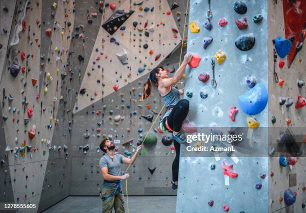 belayer kijken naar vrouwelijke sport klimmer stijgende pijler - zekeren stockfoto's en -beelden