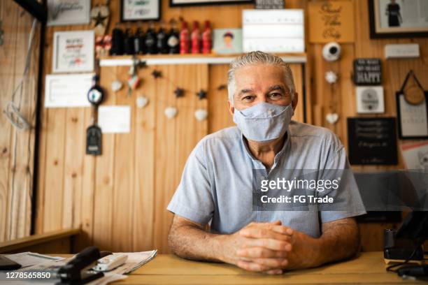 porträt eines älteren mannes mit gesichtsmaske, die in einem geschäft arbeitet - markt verkaufsstätte stock-fotos und bilder