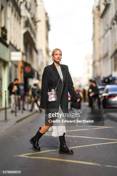 Leonie Hanne wears a black oversized blazer jacket, a grey glitter dress, a silver shiny sequined bag with attached floral designs, black leather...