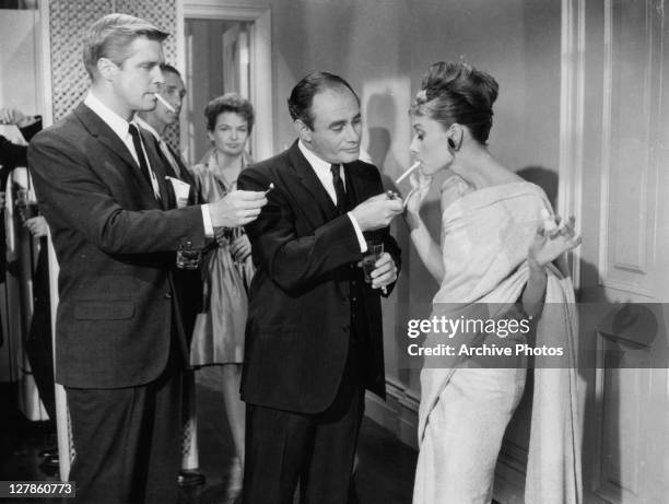 George Peppard and Martin Balsam offer to light Audrey Hepburn's cigarette in a scene from the film 'Breakfast At Tiffany's', 1961.