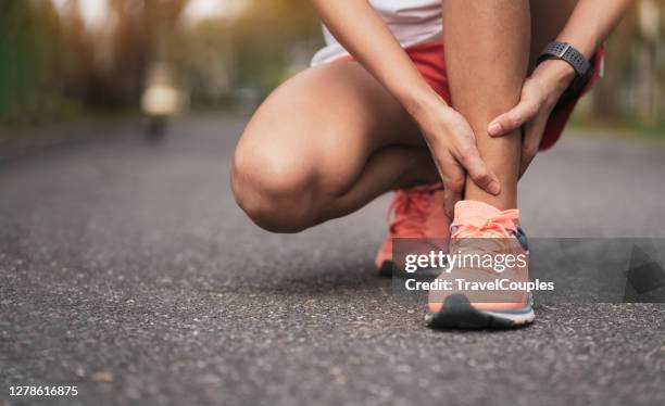 achilles injury on running outdoors. women holding achilles tendon by hands close-up and suffering with pain. ankle twist sprain accident in sport exercise running jogging. - sprain stock pictures, royalty-free photos & images