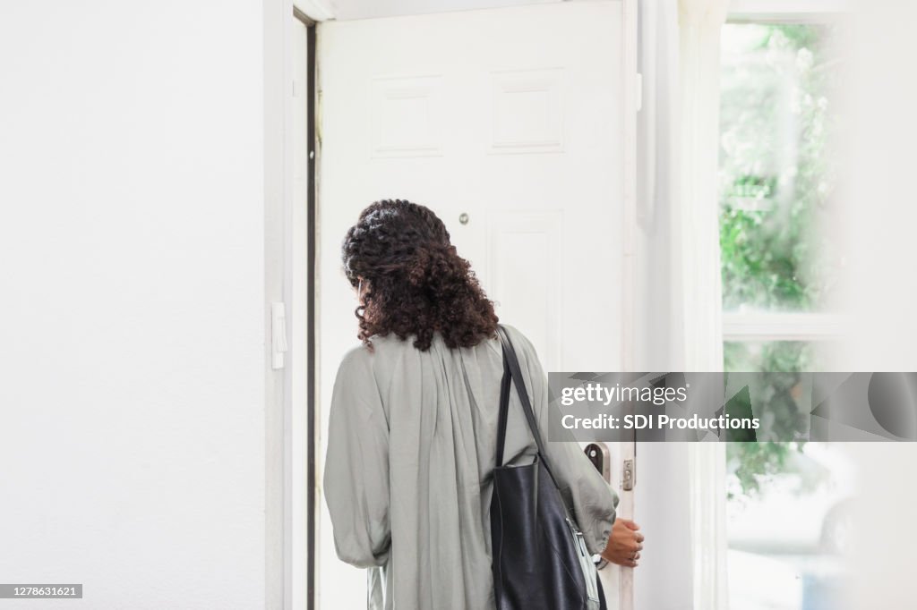 Unrecognizable young adult woman leaves house carrying purse