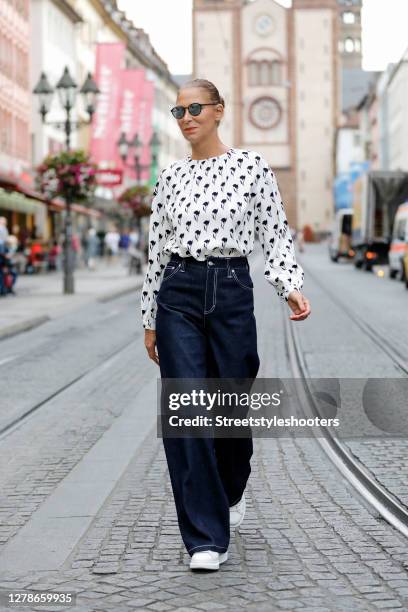 Fashion designer Eva Lutz wearing a white blouse with black flower print by Odeeh, dark blue high waisted and wide leg denim jeans by Chloe, white...