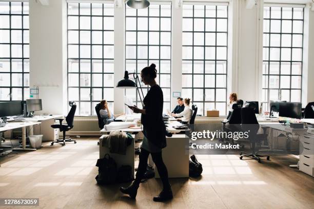 male and female business colleagues working against window in office - local de trabalho imagens e fotografias de stock