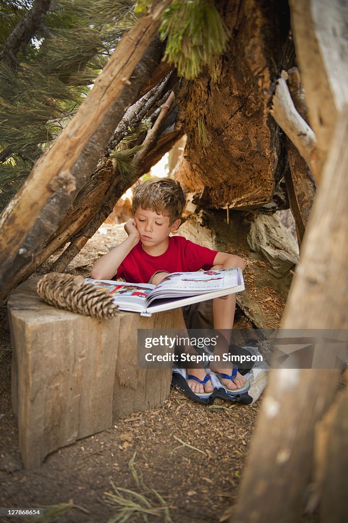 Boy reading in clubhouse made of branches