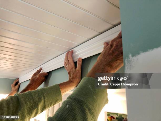 senior couple's hands together installing wood moulding inside house - amoldar fotografías e imágenes de stock