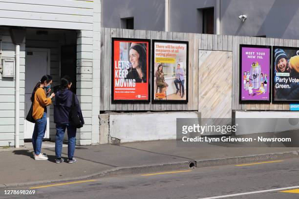 Two women, one wearing a face mask, stop on the street on 5 October 2020 by a poster of Prime Minister Jacinda Ardern, seeking re-election as leader...