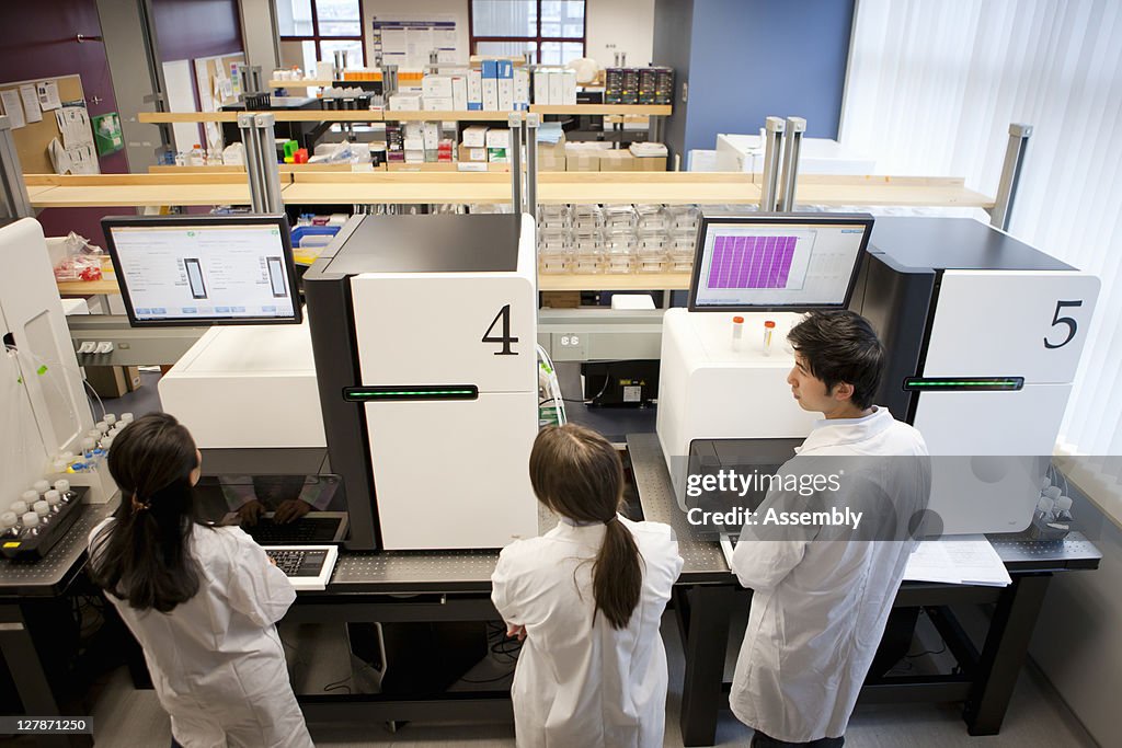 Three laboratory technicians work on computers