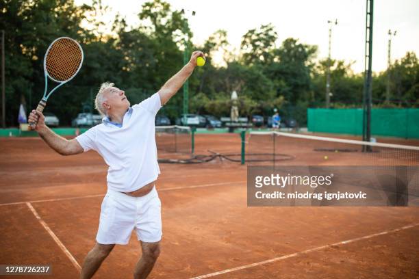 senior man serving on tennis court - senior tennis stock pictures, royalty-free photos & images