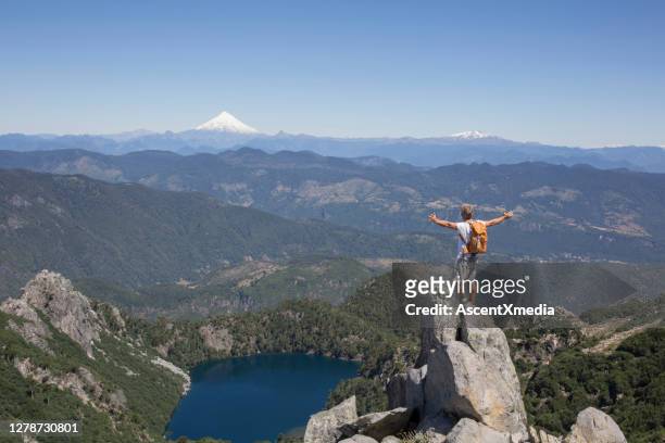hiker stands on rock pinnacle above lake and snowcapped volcano - spire stock pictures, royalty-free photos & images