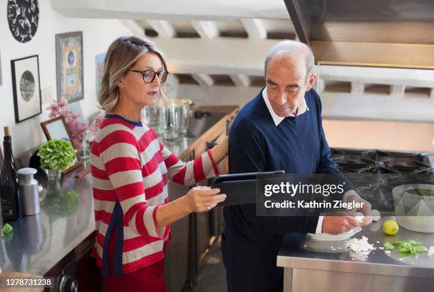 mature couple in the kitchen, looking at recipe on digital tablet - middle aged couple cooking ストックフォトと画像