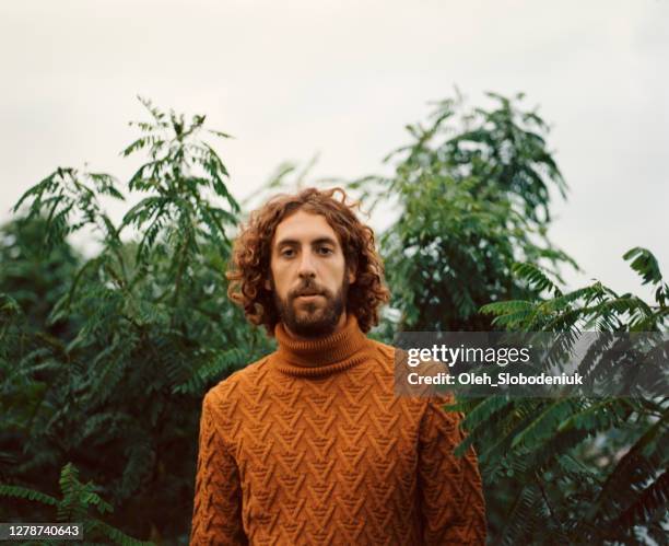 retrato del hombre con suéter naranja en el fondo de las hojas verdes - cuello alto fotografías e imágenes de stock