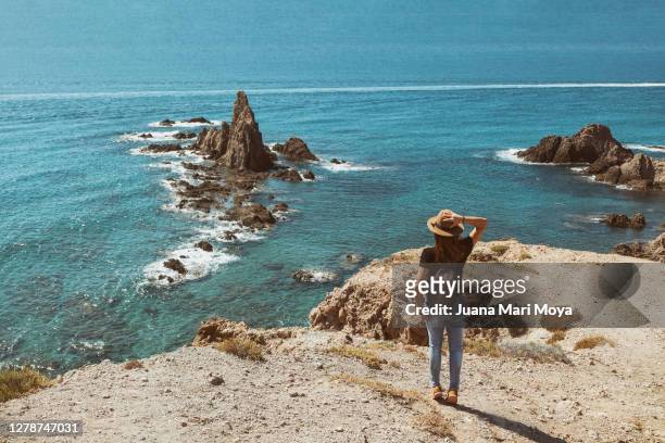 woman from behind contemplates from a cliff, the arrecife de las sirenas.  cabo de gata.  almeria.  spain - cabo de gata fotografías e imágenes de stock