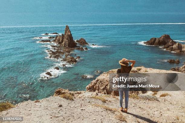 woman from behind contemplates from a cliff, the arrecife de las sirenas.  cabo de gata.  almeria.  spain - cabo de gata stock pictures, royalty-free photos & images