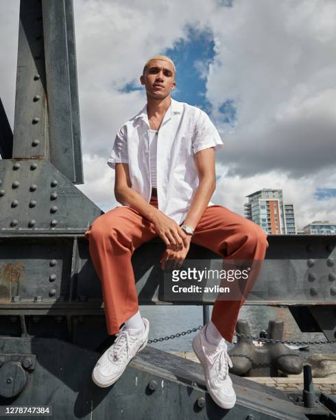 portrait of young man sitting against sky - fashion stock-fotos und bilder