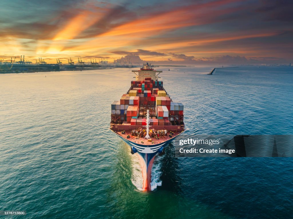 Aerial front view Container cargo ship full carrier container with terminal commercial port background for business logistics, import export, shipping or freight transportation.