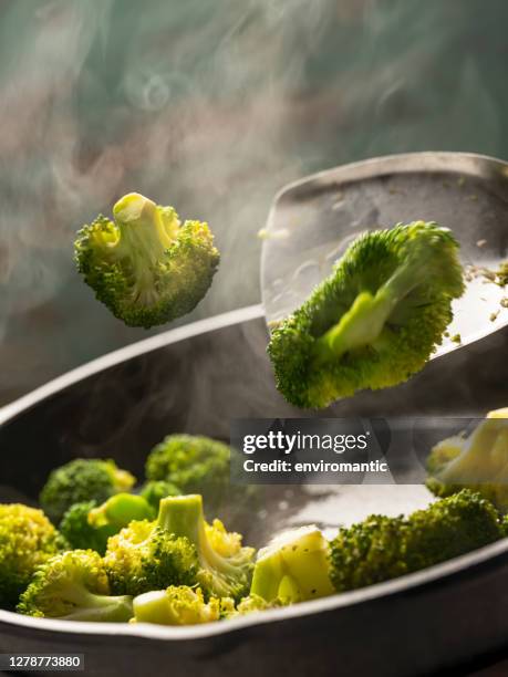 fresh broccoli spears being sauteed/stir fried in a heavy iron pan on a gas stove against a turquoise colored background. - saute stock pictures, royalty-free photos & images