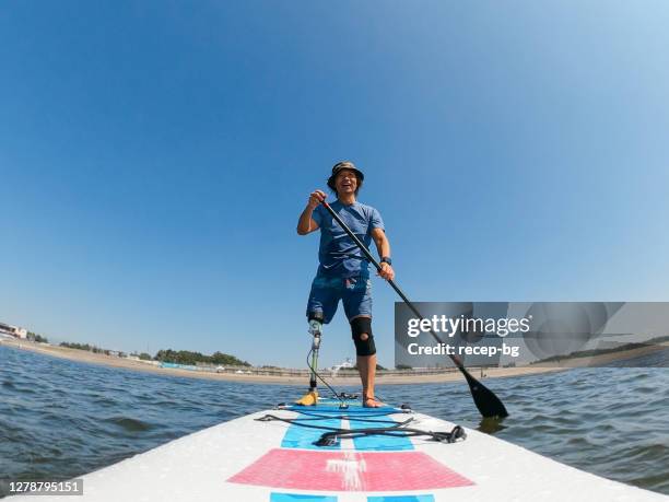 amputee man paddle boarding in sea - active seniors surfing stock pictures, royalty-free photos & images