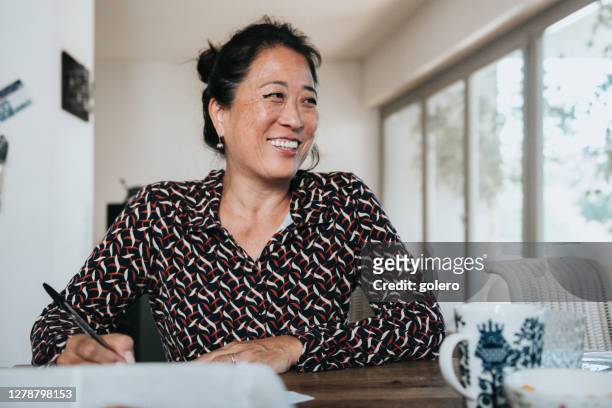 portret van glimlachende elegante vrouw die het schrijven met pen bij houten lijst werkt - vrouw 50 jaar stockfoto's en -beelden