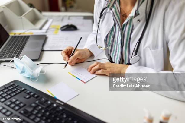 doctor making notes while on video call with patient - medical clinic stock-fotos und bilder