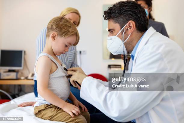 pediatrician examining boy patient with stethoscope - child coronavirus sick stock-fotos und bilder