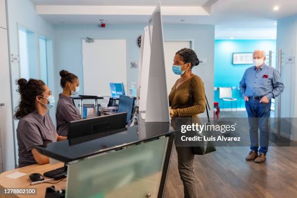 mature woman in hospital talking to the receptionist - protective face mask office stock pictures, royalty-free photos & images