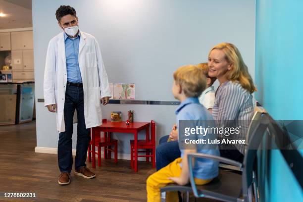 pediatrician wearing mask receiving patient in clinic - safe kids day arrivals stock pictures, royalty-free photos & images