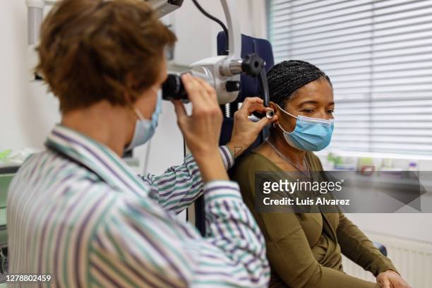 doctor examining the ear of a senior woman in clinic - ear stock pictures, royalty-free photos & images