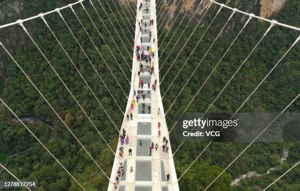 Aerial view of tourists visiting a 430-meter-long and 6-meter-wide glass bridge hanging between two steep cliffs 300 meters above the ground during...