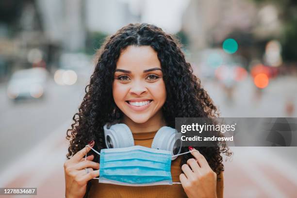 woman smiling and removing face protection mask in the city - removing surgical mask stock pictures, royalty-free photos & images