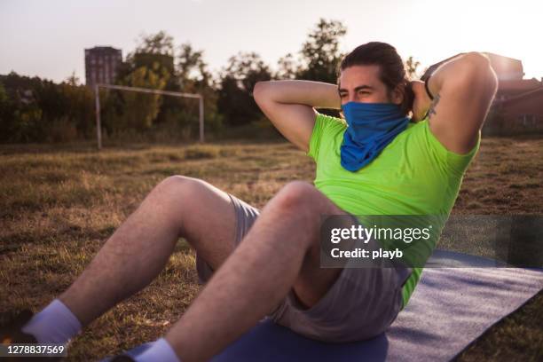 jeune homme avec le bandana faisant des crunchs à l’extérieur - buff photos et images de collection