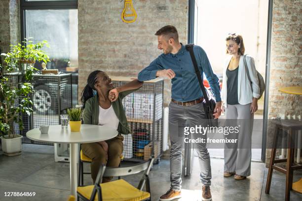 business man performing elbow bump with female colleagues after arrival in office - arrival stock pictures, royalty-free photos & images