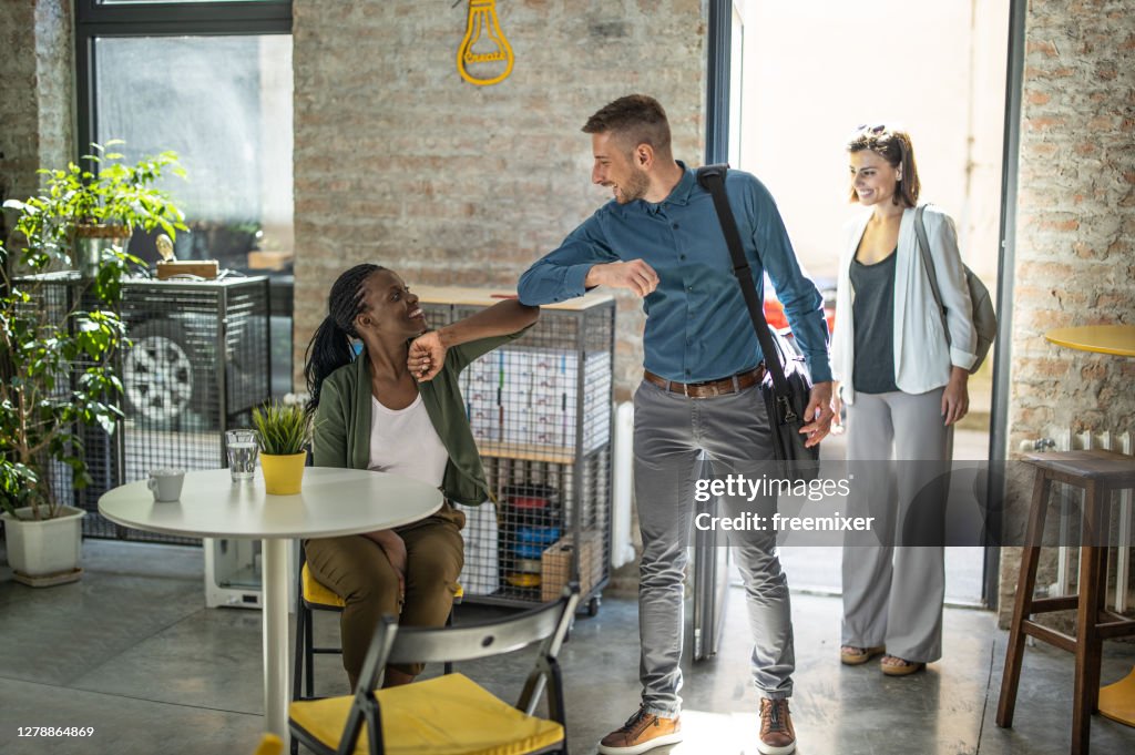 Affärsman utför armbåge bump med kvinnliga kollegor efter ankomsten till kontoret