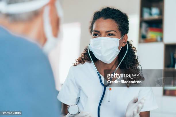 doctor visiting a senior woman at home - black glove stock pictures, royalty-free photos & images