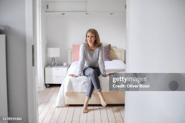 portrait of a confident mature woman sitting on bed at home - überkreuzte beine stock-fotos und bilder