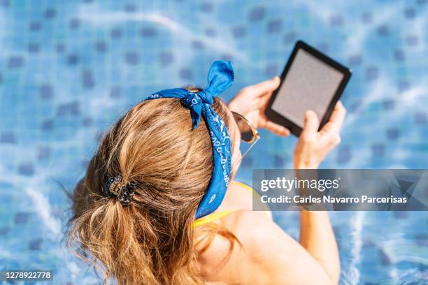 aerial view of a woman with a hair band inside a pool with an ebook. holidays concept - ereader stockfoto's en -beelden