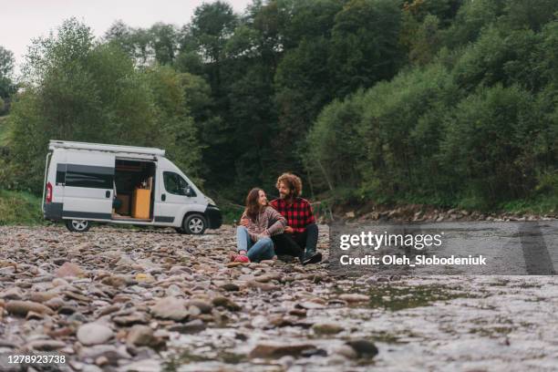 couple sitting near the camper van by the river in mountains - archival camping stock pictures, royalty-free photos & images