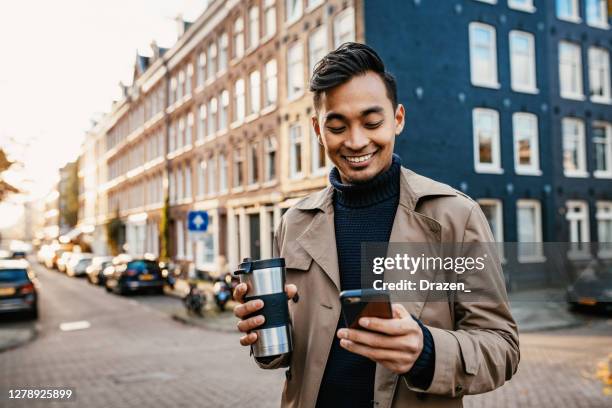 asian businessman using smart phone and drinking coffee from reusable cup - daily life in amsterdam imagens e fotografias de stock