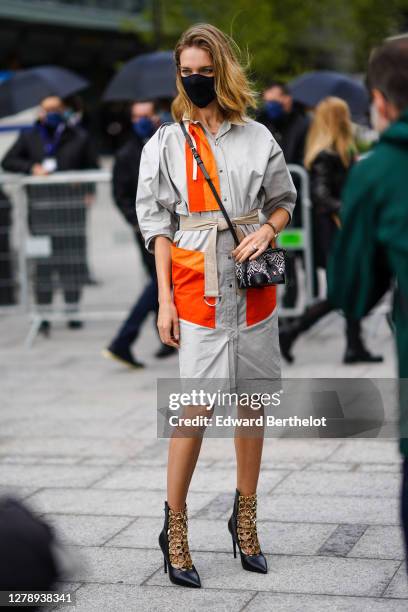 Natalia Vodianova wears a balck protective face mask, a gray and orange trench coat / dress, a Vuitton bag, black leather pointy shoes with golden...