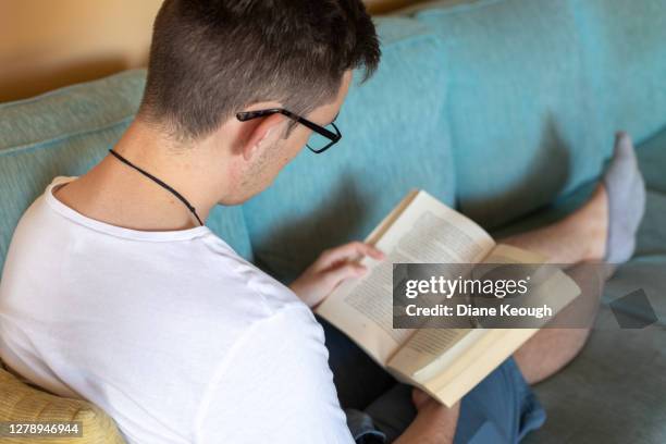 young adult boy sitting on the lounge reading book - reading glasses top view stock pictures, royalty-free photos & images